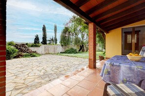 Un patio con suelo de piedra, una mesa con un frutero y una zona de estar cubierta.