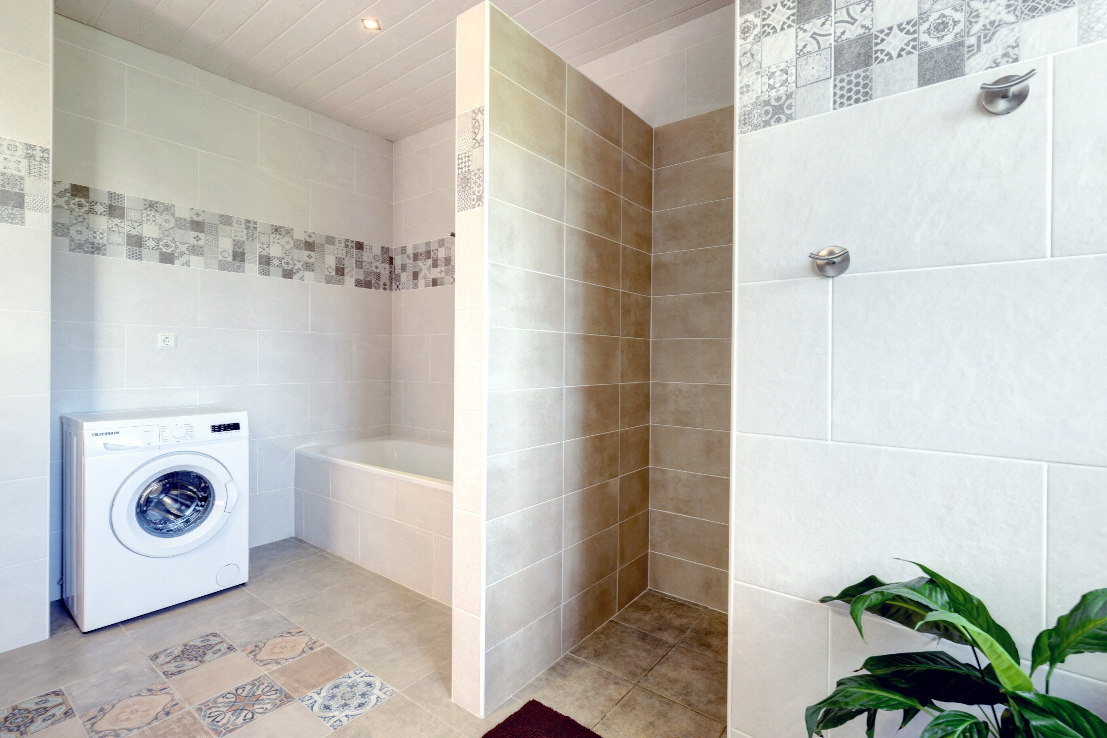 Un espace buanderie comprenant un lave-linge, une baignoire et une douche avec des murs carrelés.