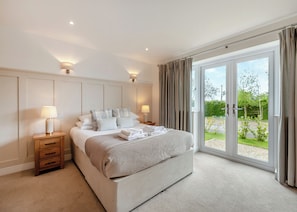 A bedroom with a large bed, two bedside tables with lamps, a view of the outdoors through a sliding glass door, and a neutral color scheme.