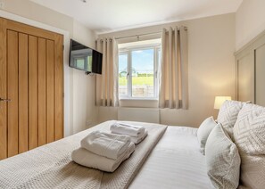 Une chambre à coucher avec un lit, un téléviseur fixé au mur, une fenêtre avec des rideaux et une porte en bois.