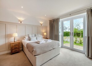 A bedroom with a large bed, two bedside tables with lamps, a view of the outdoors through a sliding glass door, and a neutral color scheme. - Luxuriously modern and spacious two storey cottage. (Glastonbury)