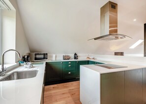 Une cuisine moderne dotée d’un four à micro-ondes, d’un grille-pain et d’une machine à café intégrés, d’un grand îlot central avec un évier et de meubles de couleur verte.