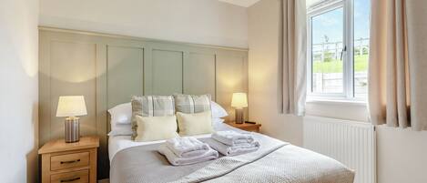 Una cama bien hecha con cabecera, dos mesitas de noche con lámparas y una ventana con cortinas.
