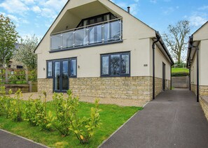 A two-story house with a stone facade, a balcony, and a paved driveway. - Luxuriously modern and spacious two storey cottage. (Glastonbury)