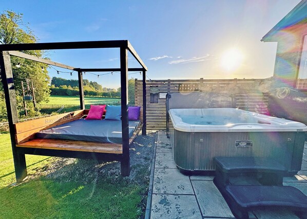 A hot tub, a wooden swing, and a wooden deck with a view of a field.