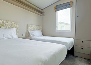 A bedroom with two beds, a window with a view, a nightstand, and a wardrobe. - 2 bedroom accommodation in Chapel St Leonards, Skegness (Chapel St Leonards, Skegness)
