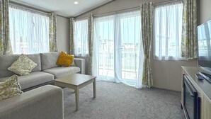 Un salon avec un canapé, une table basse, un téléviseur et de grandes fenêtres avec des rideaux.