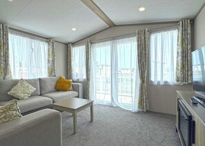 A living room with a sofa, a coffee table, a TV, and large windows with curtains.