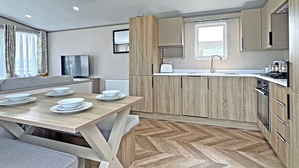 Une cuisine moderne avec des meubles en bois, un coin repas avec une table dressée pour quatre personnes et une grande fenêtre laissant entrer la lumière naturelle.