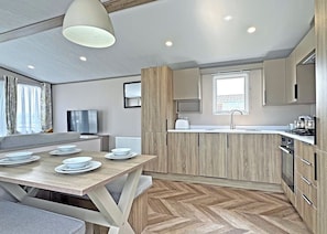 A modern kitchen with wooden cabinets, a dining area with a table set for four, and a large window providing natural light. - 2 bedroom accommodation in Chapel St Leonards, Skegness (Chapel St Leonards, Skegness)