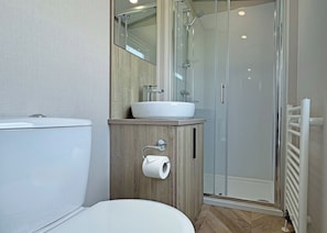 A modern bathroom with a toilet, a sink with a mirror above it, and a glass-enclosed shower area. - 2 bedroom accommodation in Chapel St Leonards, Skegness (Chapel St Leonards, Skegness)