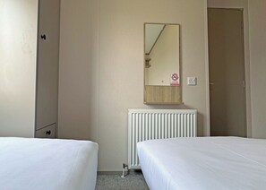 A hotel room with two beds, a radiator, a mirror, and a door.