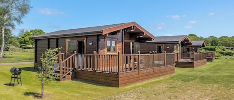 A wooden cabin with a deck, a barbecue grill, and a small tree in the yard.