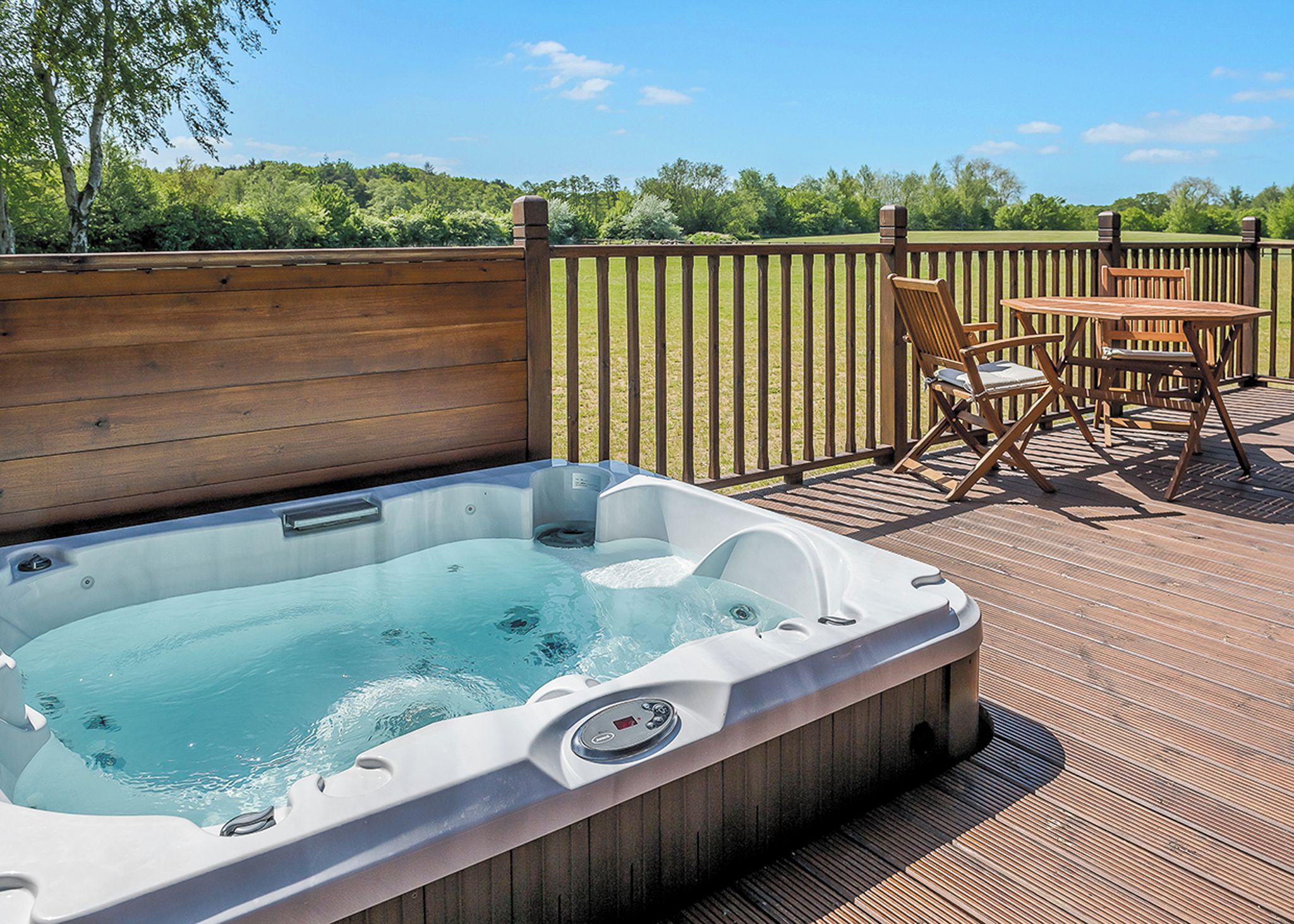A hot tub on an outdoor deck with a wooden fence and a table with chairs.