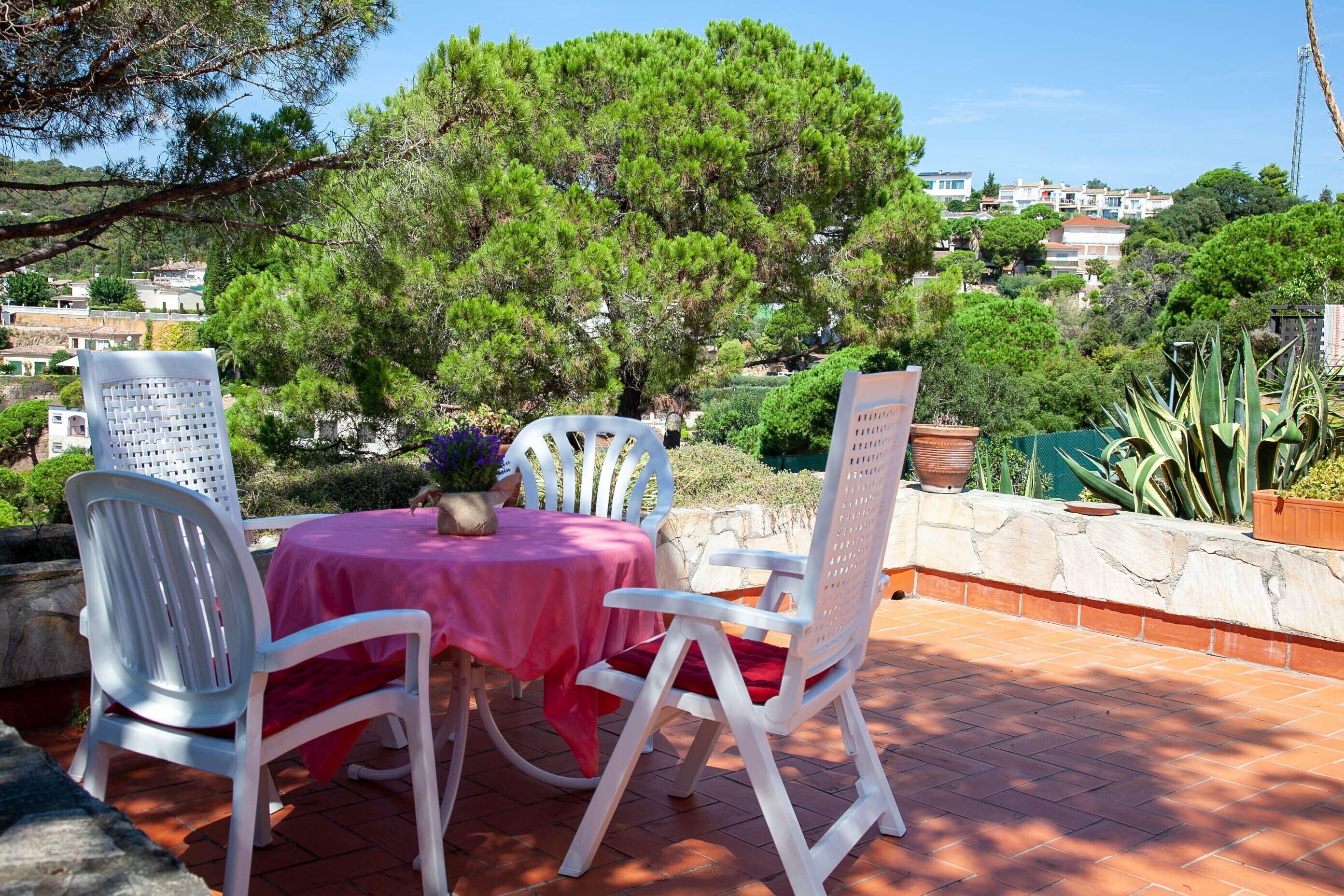 Un patio al aire libre con una mesa y sillas, rodeado de vegetación y vistas a una zona residencial.