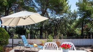 An outdoor patio with a table, chairs, a blue lounge chair, a beige umbrella, and potted plants. - Holiday Home 'Andrea' with Mountain View, Private Terrace and Wi-Fi (Tossa de Mar)