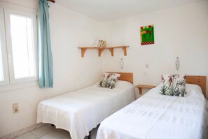 A room with two beds, a window with curtains, a shelf with books, and a wall decoration. - Holiday Home 'Andrea' with Mountain View, Private Terrace and Wi-Fi (Tossa de Mar)