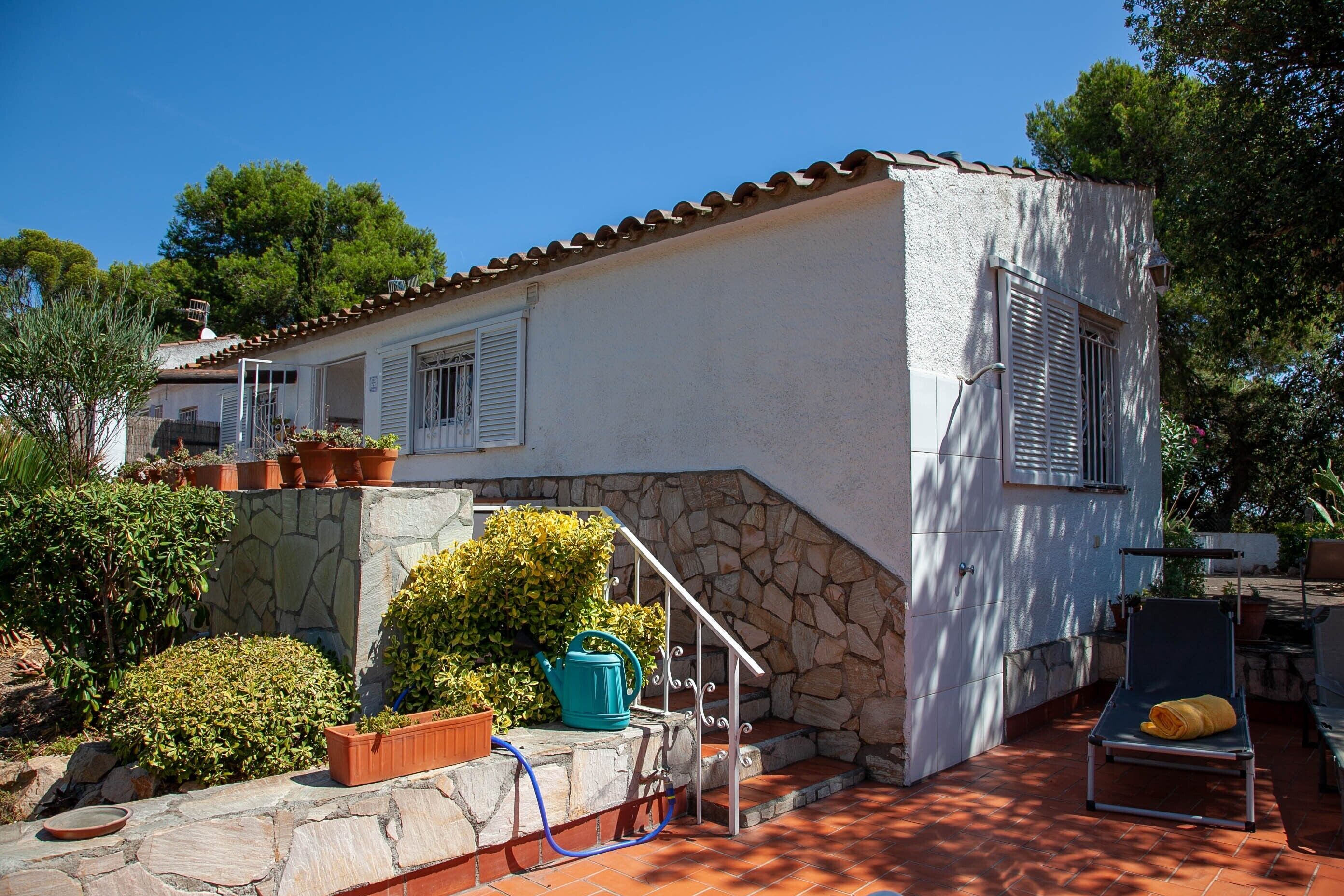 Una casa con escalones de piedra, un regador azul y una silla de lounge.