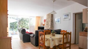 A living room with a sofa, a dining table with chairs, a stone fireplace, and a kitchen area. - Holiday Home 'Andrea' with Mountain View, Private Terrace and Wi-Fi (Tossa de Mar)