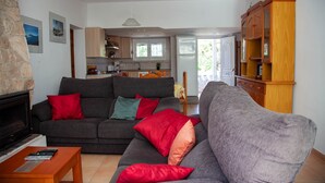 A living room with a sofa, a coffee table, and a fireplace. There is a kitchen in the background with cabinets and a refrigerator. - Holiday Home 'Andrea' with Mountain View, Private Terrace and Wi-Fi (Tossa de Mar)