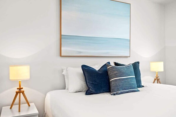 Une chambre d’hôtel avec un lit, deux tables de chevet avec des lampes et un tableau encadré au mur.