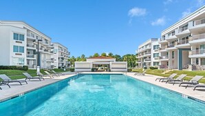 Ein Schwimmbecken mit Liegestühlen, umgeben von modernen Wohngebäuden mit Balkonen.