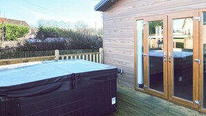A wooden deck with a hot tub, a sliding glass door, and a wooden fence.