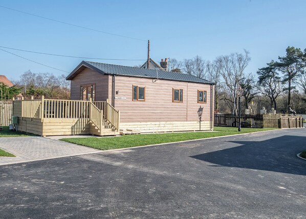 A single-story wooden building with a sloped roof, a front porch with a wooden railing, and a small front yard. - 2 bedroom accommodation in Kilwinning (Kilwinning)