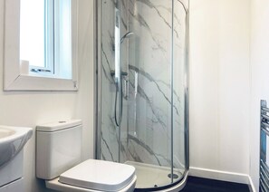 A modern bathroom with a glass-enclosed shower, a toilet, and a sink.