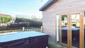 Een houten terras met een jacuzzi, een schuifpui en een houten omheining.