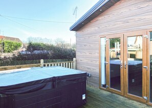 A wooden deck with a hot tub, a sliding glass door, and a wooden fence.