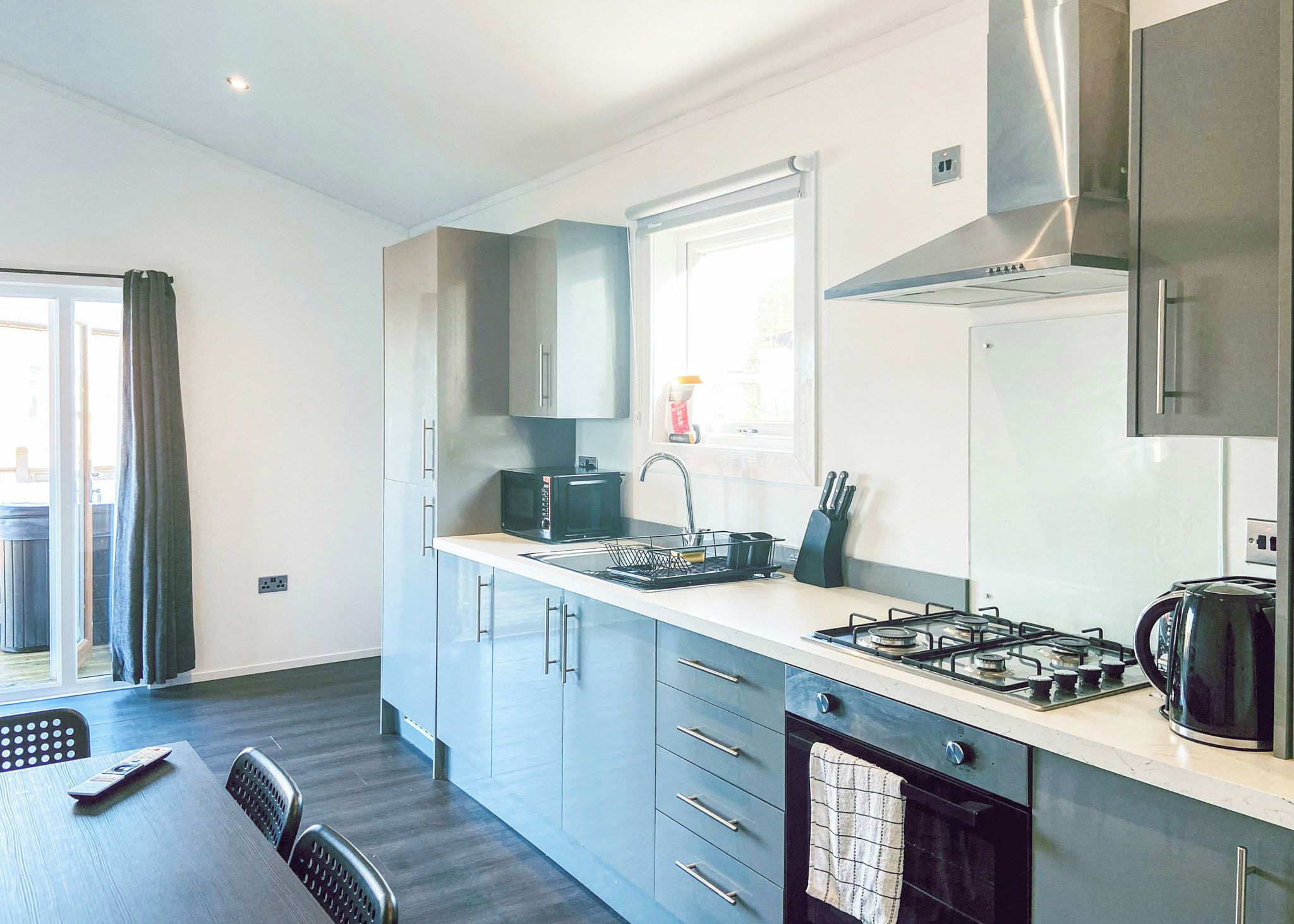 Une cuisine moderne avec des meubles gris, un micro-ondes noir, une cuisinière à gaz et une fenêtre donnant sur un beau paysage.