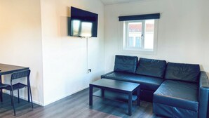 A modern living room with a sofa, a coffee table, a TV mounted on the wall, and a window with a view.