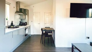 A modern kitchen with a dining area, a flat-screen TV mounted on the wall, and a wooden floor.
