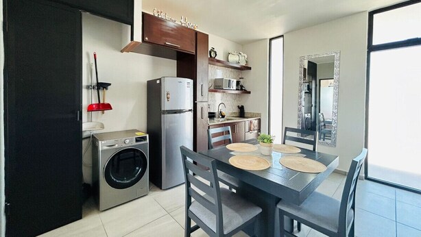 A compact kitchen with a washing machine, a refrigerator, and a dining area with a table and chairs.