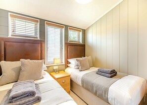 A hotel room with two beds, a nightstand, a lamp, and a window with blinds. - Luxurious lodge with vaulted ceilings and a welcoming feature fireplace. (Glastonbury)