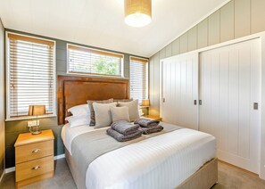 A bedroom with a bed, bedside tables, a wardrobe, and a window with blinds. - Luxurious lodge with vaulted ceilings and a welcoming feature fireplace. (Glastonbury)