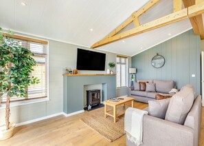 A living room with a fireplace, sofa, coffee table, and a TV mounted above the fireplace. - Luxurious lodge with vaulted ceilings and a welcoming feature fireplace. (Glastonbury)