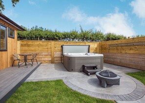 Un patio trasero con un jacuzzi, un pozo de fuego y una mesa de patio con sillas.