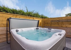 A hot tub in an outdoor setting with a wooden deck and a wooden fence in the background. - Luxurious lodge with vaulted ceilings and a welcoming feature fireplace. (Glastonbury)