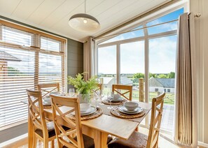 A dining area with a table set for four, large windows, and a view of the countryside. - Luxurious lodge with vaulted ceilings and a welcoming feature fireplace. (Glastonbury)