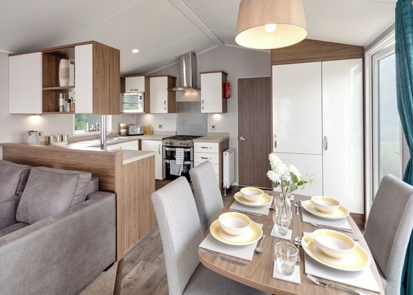 A modern kitchenette with a microwave, stove, and oven. There is a dining area with a table set for four, including plates, glasses, and cutlery.