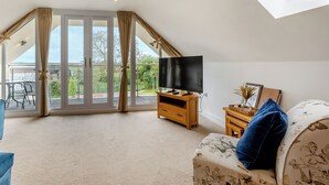 A spacious living room with a large TV, a sofa, and a balcony with curtains. - Outstanding and beautifully presented first floor apartment. (Glastonbury)