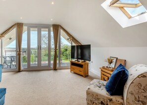 A spacious living room with a large TV, a sofa, and a balcony with curtains. - Outstanding and beautifully presented first floor apartment. (Glastonbury)