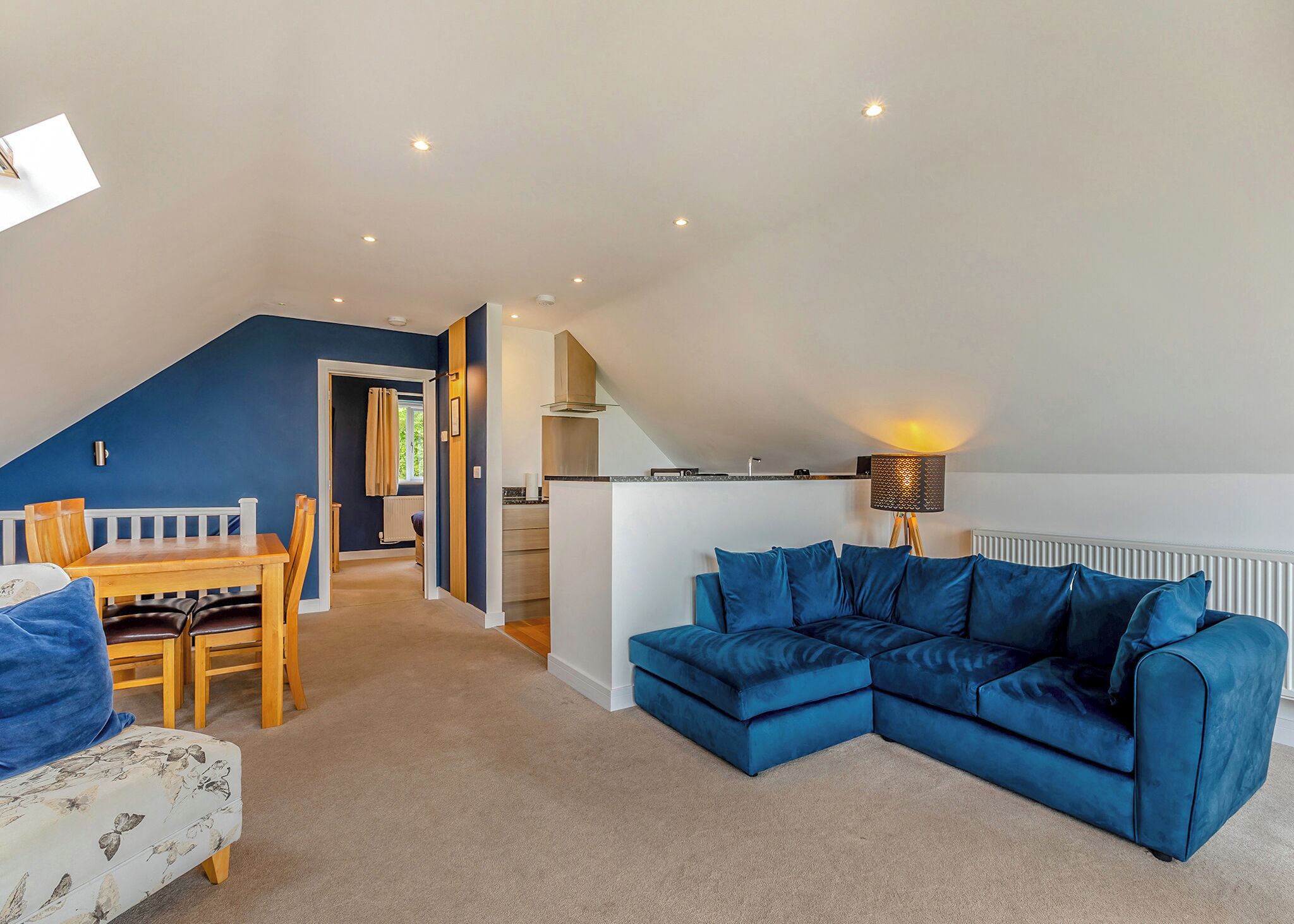 A loft-style living space with a dining area, a blue sectional sofa, a kitchen, and a staircase.