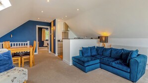 A loft-style living space with a dining area, a blue sectional sofa, a kitchen, and a staircase. - Outstanding and beautifully presented first floor apartment. (Glastonbury)