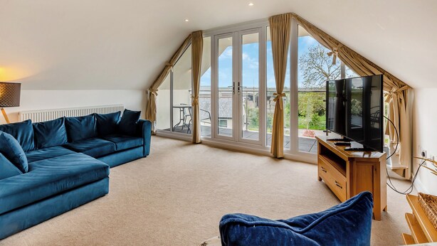A spacious loft bedroom with a large window, a television, a sofa, and a wooden dresser. - Outstanding and beautifully presented first floor apartment. (Glastonbury)