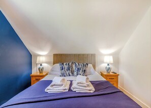 A hotel room with a bed, two bedside tables, a headboard, and a blue accent wall.