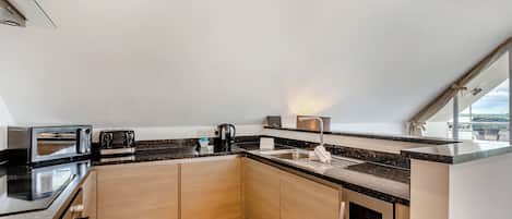 A modern kitchen with built-in appliances, a sink, and a window overlooking a landscape.