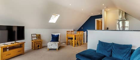 A living room with a TV, a sofa, a dining table with chairs, a small table with a chair, and a kitchen area with a stove.